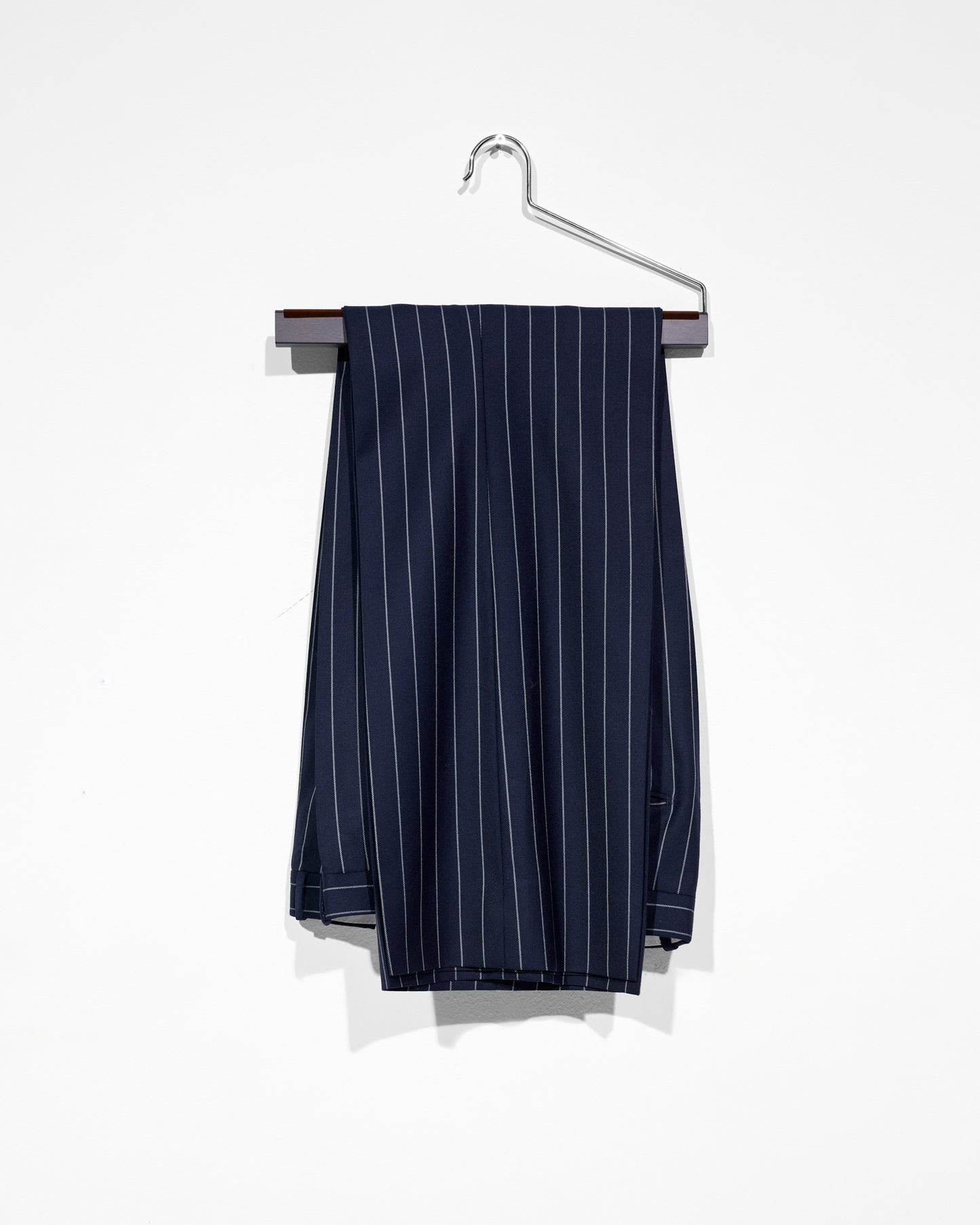 Navy pinstripe pants on a hanger against a white background