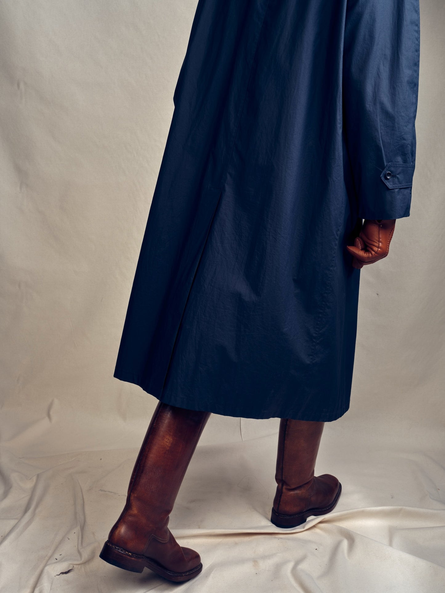 Person wearing a long navy Turnbull & Asser car coat in cotton and brown boots on a plain background