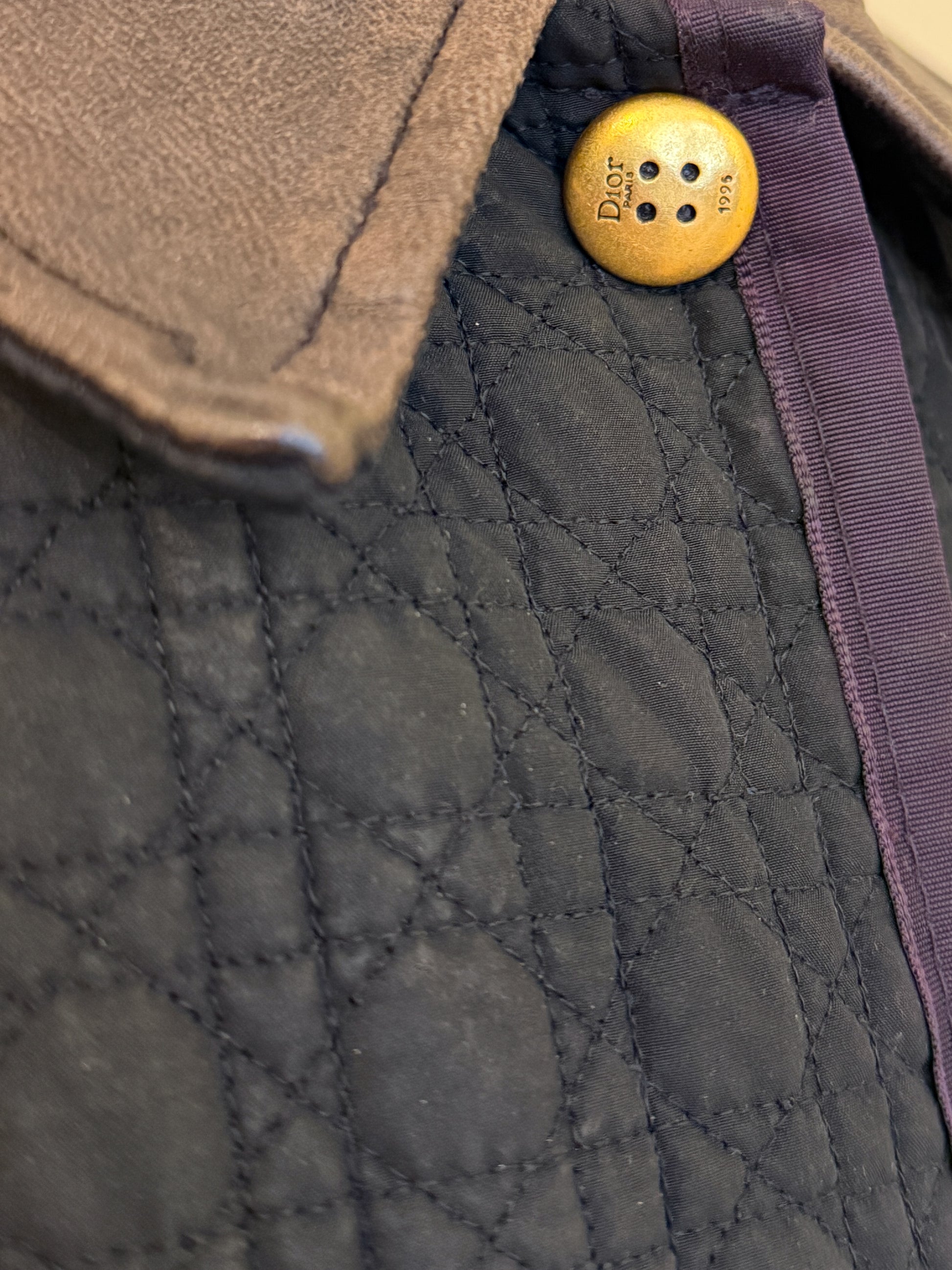 Close-up of a textured Dior jacket with a gold button featuring text.